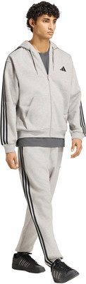 Mann im grauen Adidas-Anzug mit schwarzen Streifen und Turnschuhen.