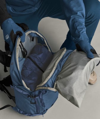 Eine Person packt einen blauen Rucksack mit einer Jacke. Eine Person packt einen blauen Rucksack mit einer Jacke.