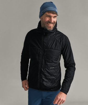 Ein Mann in einer schwarzen Kapuzenjacke und einer blauen Mütze lächelt.