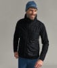 Ein Mann in einer schwarzen Kapuzenjacke und einer blauen Mütze lächelt.