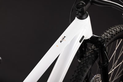 Detail eines weißen Mountainbike-Rahmens mit AIM-Logo und Vorderradgabel.