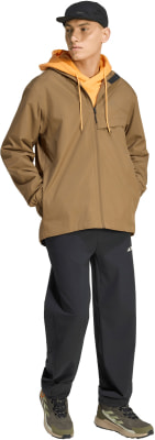 Ein Mann in einer braunen Jacke, einem orangefarbenen Kapuzenpullover und einer schwarzen Hose.
