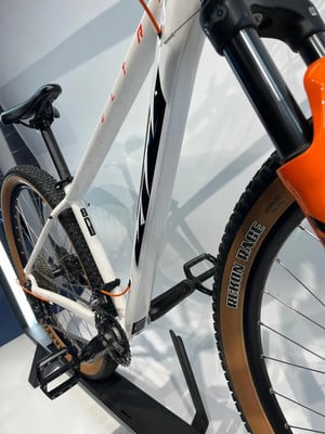 Detail eines weißen Mountainbikes mit orangefarbenen Akzenten und Reifenbeschriftung. Detail eines weißen Mountainbikes mit orangefarbenen Akzenten und Reifenbeschriftung.