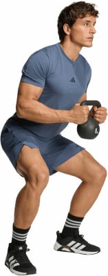 Ein Mann in blauem Shirt und Shorts macht Kniebeugen mit Kettlebell. Ein Mann in blauem Shirt und Shorts macht Kniebeugen mit Kettlebell.