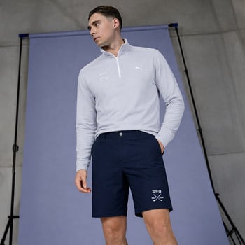 Ein Mann in einem grauen Langarmshirt und dunkelblauen Shorts posiert.