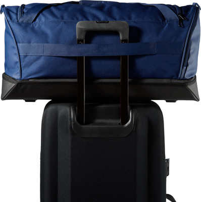 Eine blaue Reisetasche liegt auf einem schwarzen Koffer mit ausgefahrenem Griff. Eine blaue Reisetasche liegt auf einem schwarzen Koffer mit ausgefahrenem Griff.