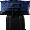 Eine blaue Reisetasche liegt auf einem schwarzen Koffer mit ausgefahrenem Griff.