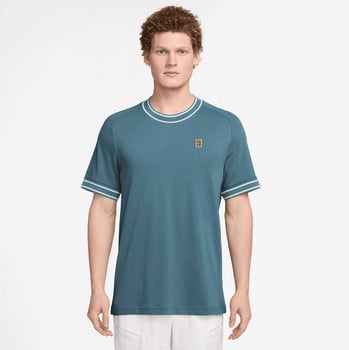 Mann in einem blaugrünen T-Shirt mit weißem Besatz und Logo auf der Brust.
