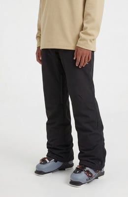 Ein Mann in schwarzer Skihose und beige Pullover mit Skischuhen.