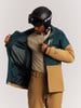 Ein Mann in einer Skijacke und einem Helm betrachtet die Innentaschen der Jacke.