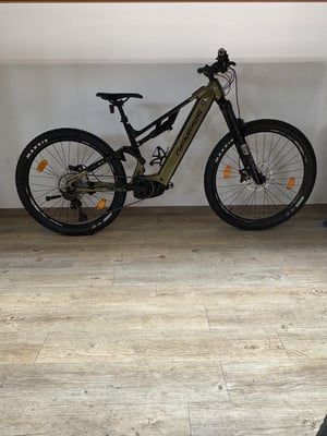 Ein olivgrünes Genesis E-Mountainbike steht auf einem Holzboden.