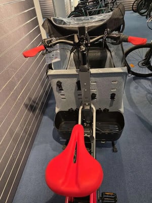 Ein roter Sattel und Lenker auf einem Lastenfahrrad mit grauem Korb. Ein roter Sattel und Lenker auf einem Lastenfahrrad mit grauem Korb.