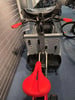 Ein roter Sattel und Lenker auf einem Lastenfahrrad mit grauem Korb.