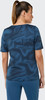 Eine Frau in einem blauen T-Shirt mit abstraktem Muster und blauen Hosen.