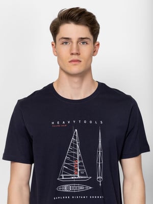 Egy férfi sötétkék pólóban, vitorlás grafikával és HEAVY TOOLS felirattal. Egy férfi sötétkék pólóban, vitorlás grafikával és HEAVY TOOLS felirattal.