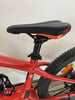 Ein rotes Mountainbike mit schwarzem Sattel und orangen Details, Nahaufnahme.