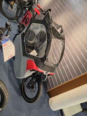 Ein Lastenrad mit Verdeck für Kinder steht auf einem blauen Teppich. Ein Lastenrad mit Verdeck für Kinder steht auf einem blauen Teppich.