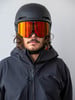 Ein Mann in einem Skianzug mit Helm und roten Spiegelski-Brillen vor grauem Hintergrund.