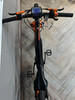 Ein schwarzes E-Bike mit orangefarbenen Details und Digitalanzeige steht an einer Wand.