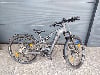 Graues Focus E-Bike mit Schutzblechen und Gepäckträger vor grauem Hintergrund.