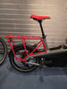 Roter Sattel und Gepäckträger an einem E-Bike vor einer Metallwand.
