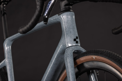Vorderseite eines grauen Gravelbikes mit schwarzem Logo und braunem Reifen. Vorderseite eines grauen Gravelbikes mit schwarzem Logo und braunem Reifen.