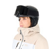 Eine Frau in einem Skischutzhelm und Brille, bekleidet mit einer beige Jacke.