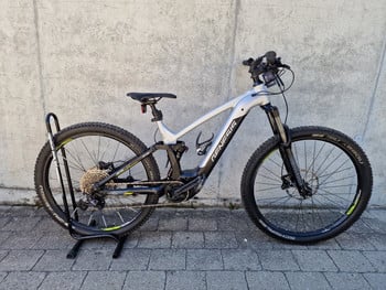 Silbernes Genesis E-Bike auf einem Ständer vor einer Betonwand.