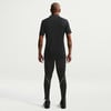 Ein Mann in einem schwarzen Poloshirt und Hose mit weißer Paspel steht mit dem Rücken zur Kamera.