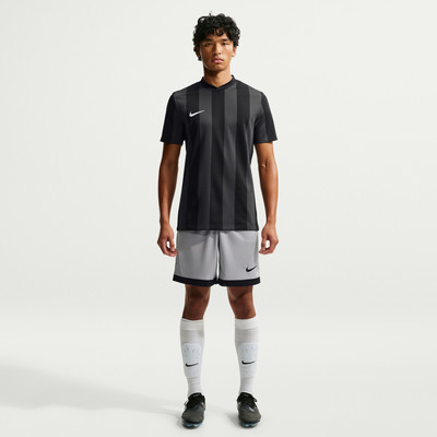 Ein Mann in einem schwarzen Streifen-Trikot und grauen Shorts steht vor weißem Hintergrund.