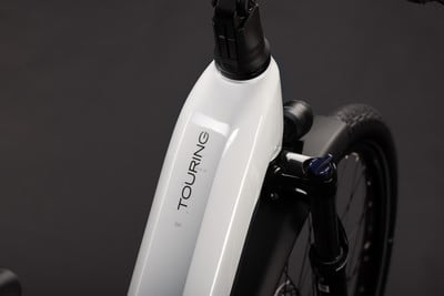 Detail eines weißen E-Bikes mit der Aufschrift TOURING und Vorderradgabel. Detail eines weißen E-Bikes mit der Aufschrift TOURING und Vorderradgabel.