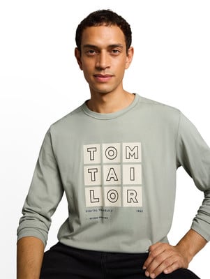 Egy férfi zöld hosszú ujjú pólóban, Tom Tailor felirattal. Egy férfi zöld hosszú ujjú pólóban, Tom Tailor felirattal.