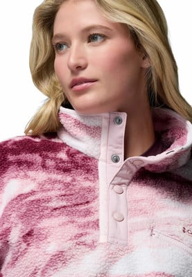 Dívka s blond vlasy má na sobě růžovou fleecovou bundu s barevným vzorem. Dívka s blond vlasy má na sobě růžovou fleecovou bundu s barevným vzorem.