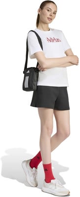 Model in weißem T-Shirt, schwarzer Hose und roten Socken mit Tasche.