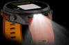 Eine Smartwatch mit orangefarbenem Armband und eingeschaltetem Licht.