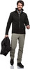 Ein Mann in schwarzer Jacke und beiger Hose hält eine schwarze Jacke in der Hand.