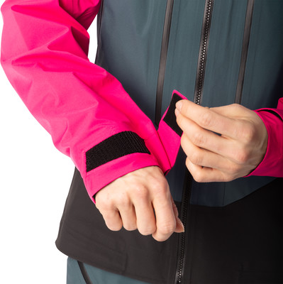 Eine Frau schließt den Klettverschluss am Ärmel einer pink-grauen Jacke.