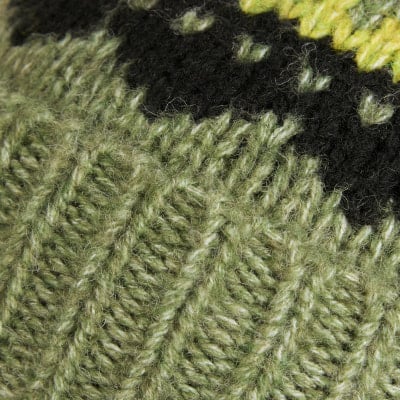 Detail eines Strickmusters in Grün- und Schwarztönen mit unregelmäßigen hellen Punkten. Detail eines Strickmusters in Grün- und Schwarztönen mit unregelmäßigen hellen Punkten.
