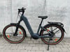 Ein graues E-Bike mit schwarzen Akzenten steht auf einem Gehweg vor einer Wand.