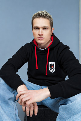 Junger Mann mit blonden Haaren in einem schwarzen Kapuzenpullover mit roten Kordeln. Junger Mann mit blonden Haaren in einem schwarzen Kapuzenpullover mit roten Kordeln.