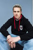 Junger Mann mit blonden Haaren in einem schwarzen Kapuzenpullover mit roten Kordeln.