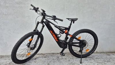 Ein schwarzes KTM E-Mountainbike mit orangefarbenen Akzenten steht an einer Wand. Ein schwarzes KTM E-Mountainbike mit orangefarbenen Akzenten steht an einer Wand.