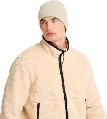 Ein Mann trägt eine cremefarbene Fleecejacke und eine Mütze.