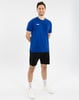 Ein junger Mann in einem blauen T-Shirt und schwarzen Shorts steht mit verschränkten Händen.