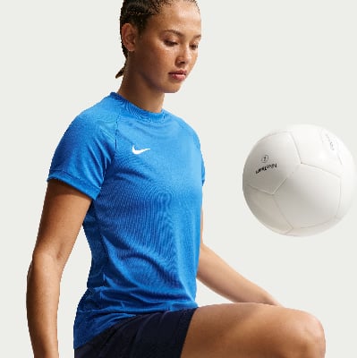 Frau in blauem Shirt und dunklen Shorts mit Ball.