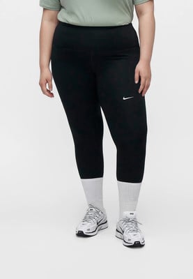 Modelka v černých legínách Nike a bílých teniskách stojí na bílém pozadí. Modelka v černých legínách Nike a bílých teniskách stojí na bílém pozadí.