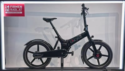 Ein schwarzes GoCycle-Elektrofahrrad steht mit einem Schild links ausgestellt. Ein schwarzes GoCycle-Elektrofahrrad steht mit einem Schild links ausgestellt.