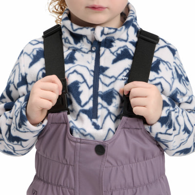 Kind in einem Overall mit einem Fleece-Pullover mit Bergedruck.