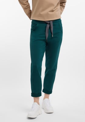 Dunkelgrüne Damenhose mit grauem Kordelzug und weißen Sneakern. Dunkelgrüne Damenhose mit grauem Kordelzug und weißen Sneakern.