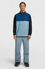 Ein Mann in einem blauen Fleece-Pullover und grauer Hose posiert vor hellem Hintergrund.